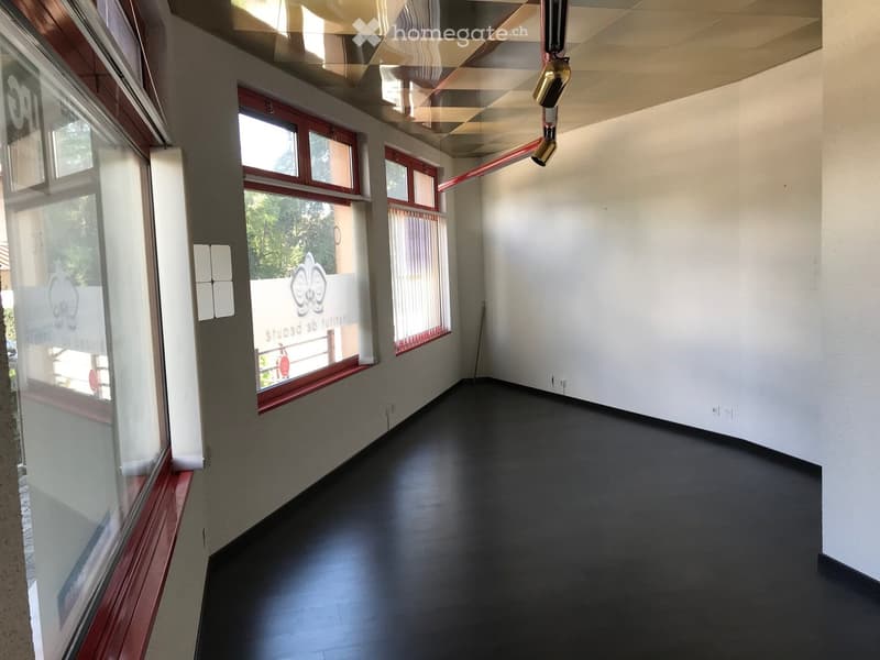 Empty room with white walls, black floor, three windows with red frames, ceiling with lights