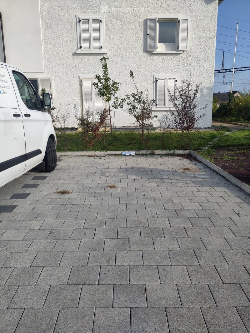 white exterior house with 4 windows and white shutters, paved parking area