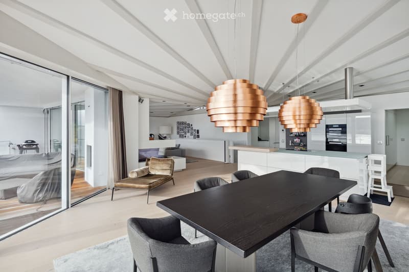Dining room with large windows, modern furniture, wooden floor, copper pendant lights, kitchen island, and a view of the outside