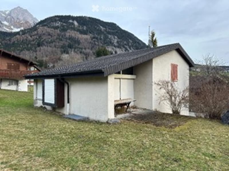 small white house, black roof, raised ground floor, wooden bench, mountain in the background