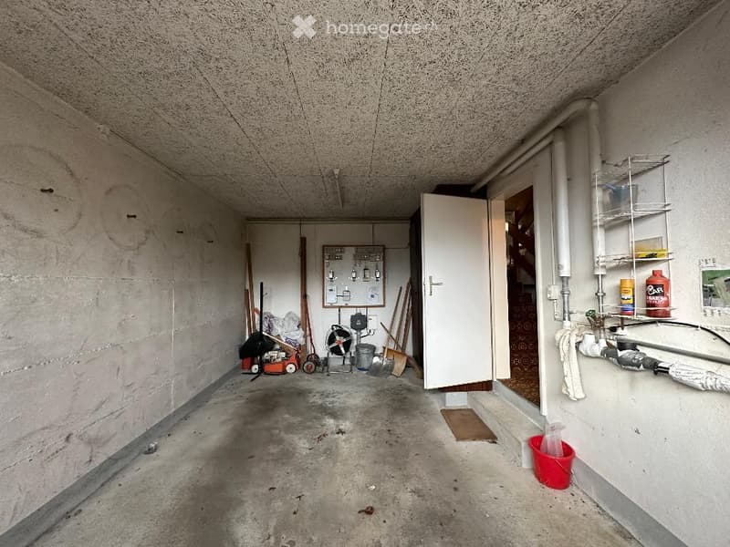 empty garage with concrete floor, white walls, open door, storage items, tools, buckets, pipes