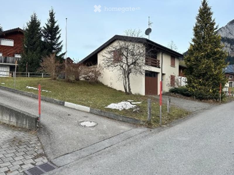 Detached house, white exterior, brown garage, driveway, trees, grass, mountains in the background