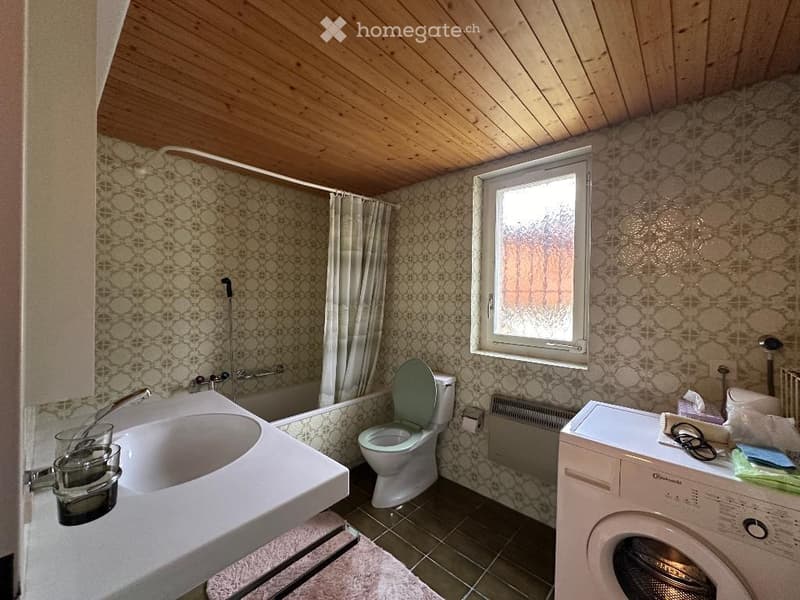 Bathroom with bathtub, toilet, sink, washing machine, wooden ceiling, tiled walls, window