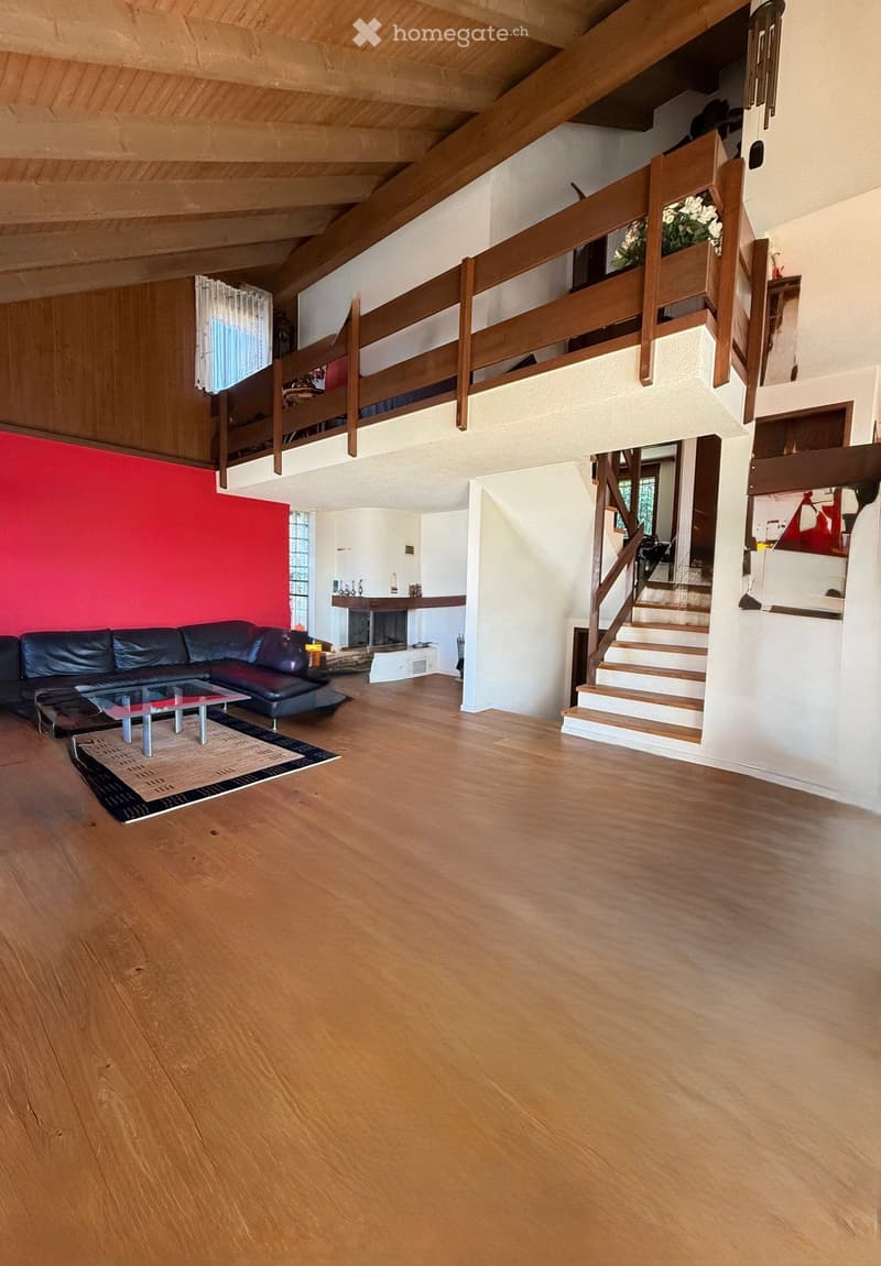 large living room, wooden floor, red accent wall, black leather couch, glass coffee table, balcony with wooden railings, fireplace