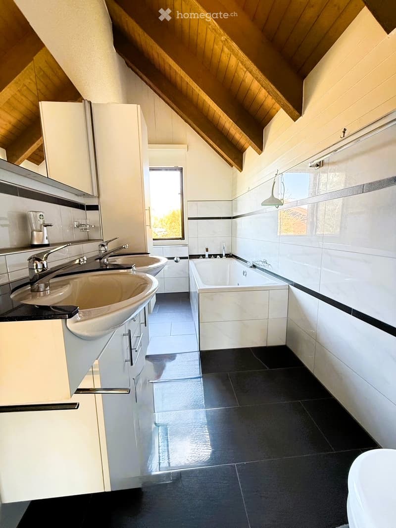 Modern bathroom with black tiles, white vanity, bathtub, and double sink with silver faucets