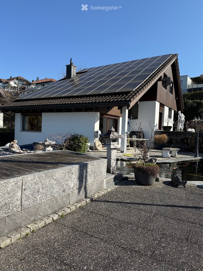 2 story house, white exterior, brown roof, solar panels, wooden deck, garden, outdoor sitting area, outdoor dining area, small pond, lanterns