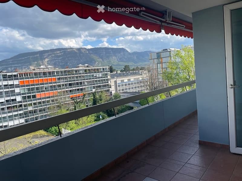 Balcony with tiled floor, metal railing, red awning, and a view of the city and mountains