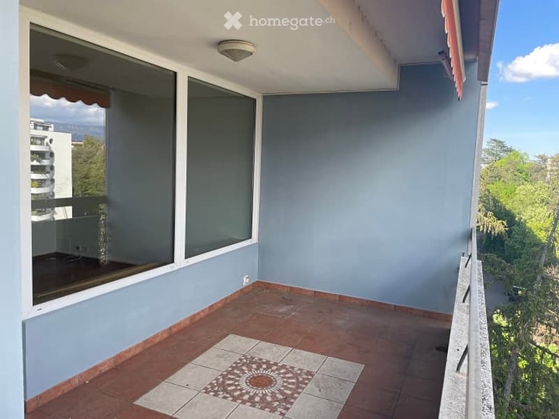 Balcony with tiled floor, large windows, view of trees and buildings