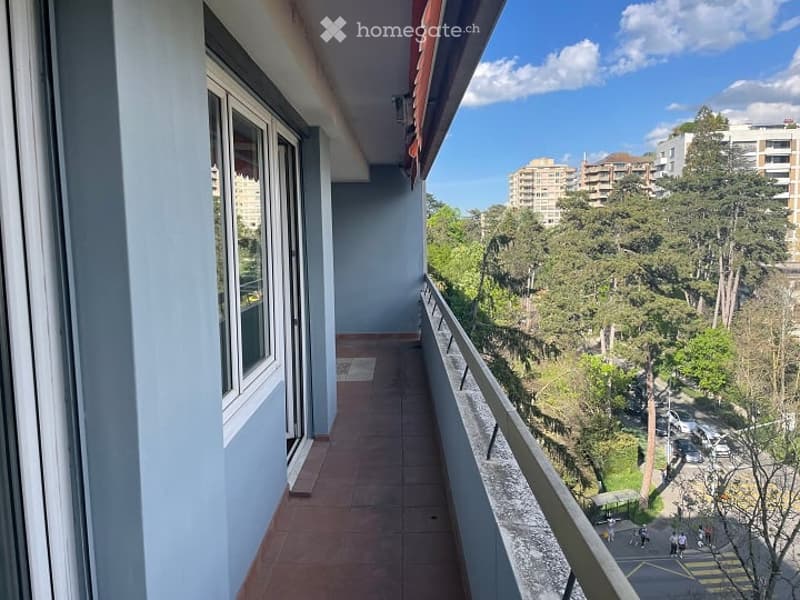 Balcony with tiled floor, metal railing, glass door, and windows, overlooking a street with trees and buildings