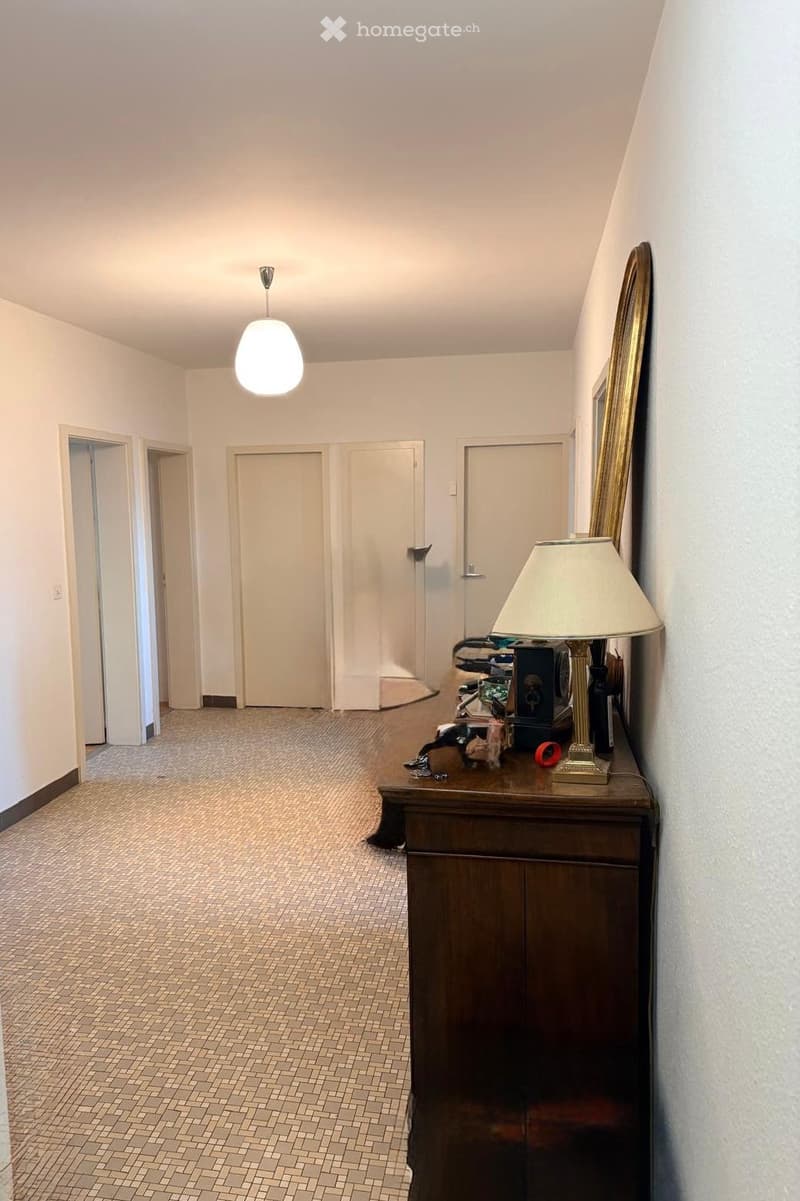 Empty hallway with white walls, tiled floor, white doors, a lamp, and a wooden cabinet with a lamp on top