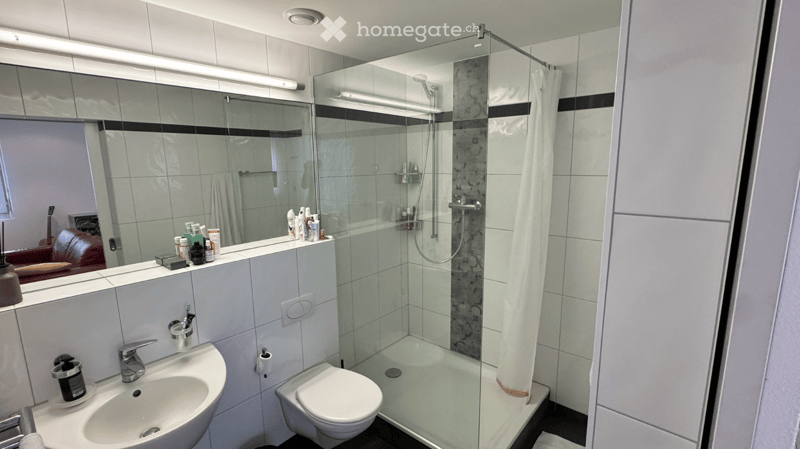white tiles, glass shower, white sink, white toilet, mirror, toiletries