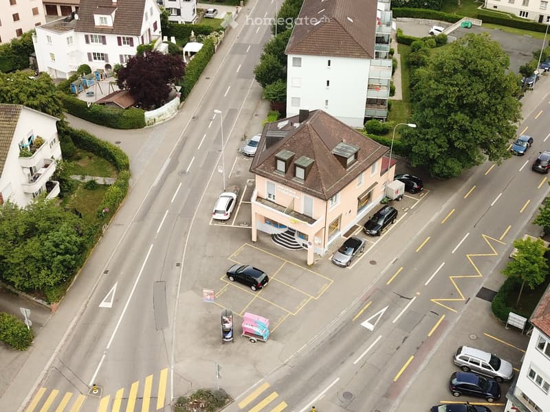 Aerial view of a street with multiple buildings, parking lot, and cars parked in front of a building