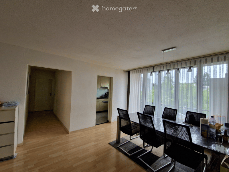 Dining room, hardwood floor, large windows, dining table with chairs, kitchen visible through the doorway, white walls, ceiling lights