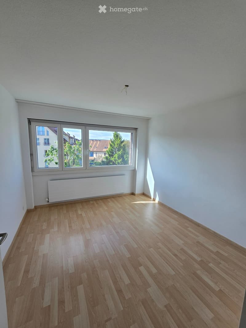 Empty room with wooden flooring, white walls, large windows, and a radiator. No furniture or equipment present.