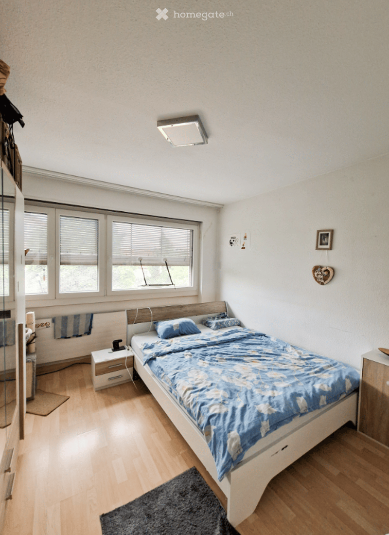 White wooden floor, single bed with blue sheets, two bedside tables, large windows, lamps, white walls
