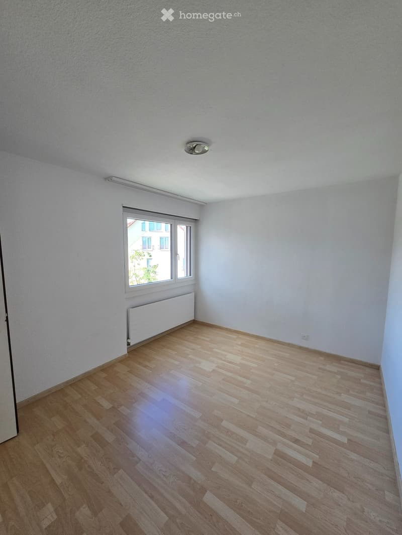 Empty room with wooden flooring, white walls, a window with a radiator below, and a ceiling light fixture.
