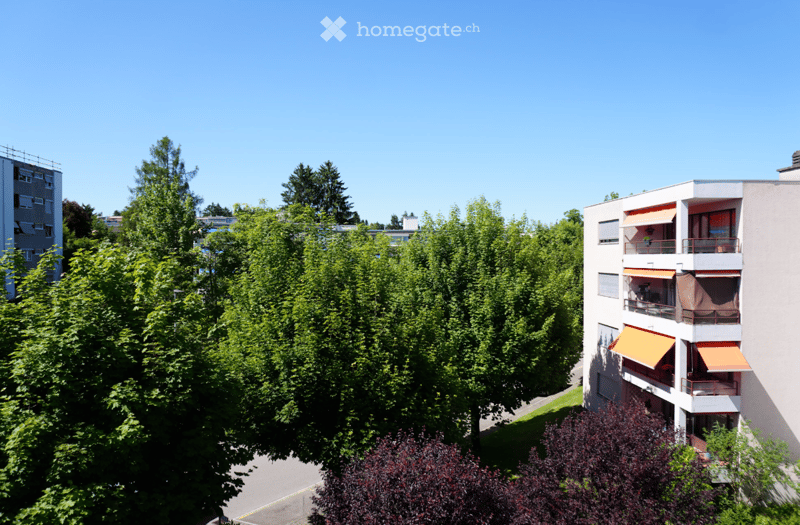 Apartment building with balconies, surrounded by trees and greenery