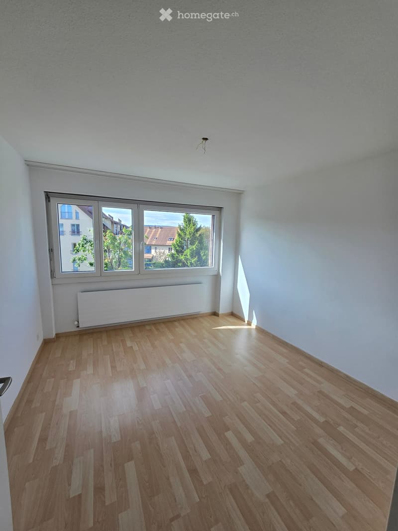 Empty room with wooden flooring, white walls, large windows, and a radiator below the windows.