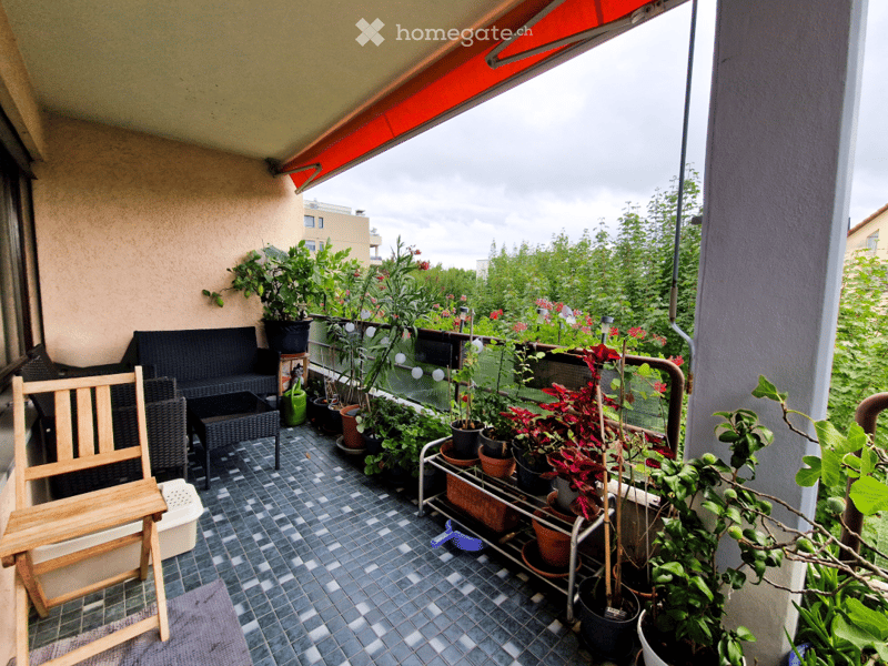 covered balcony, wooden chair, black wicker furniture, tiled floor, plants and flowers in pots