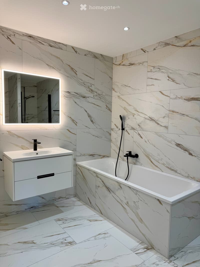 modern bathroom with white marble tiles, white vanity, bathtub, mirror, and black fixtures
