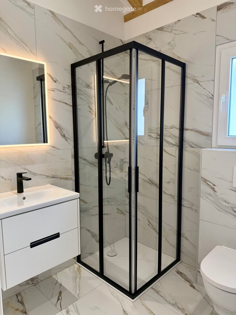 Modern bathroom with marble tiles, glass shower enclosure, white vanity, black faucet, mirror, and white toilet.