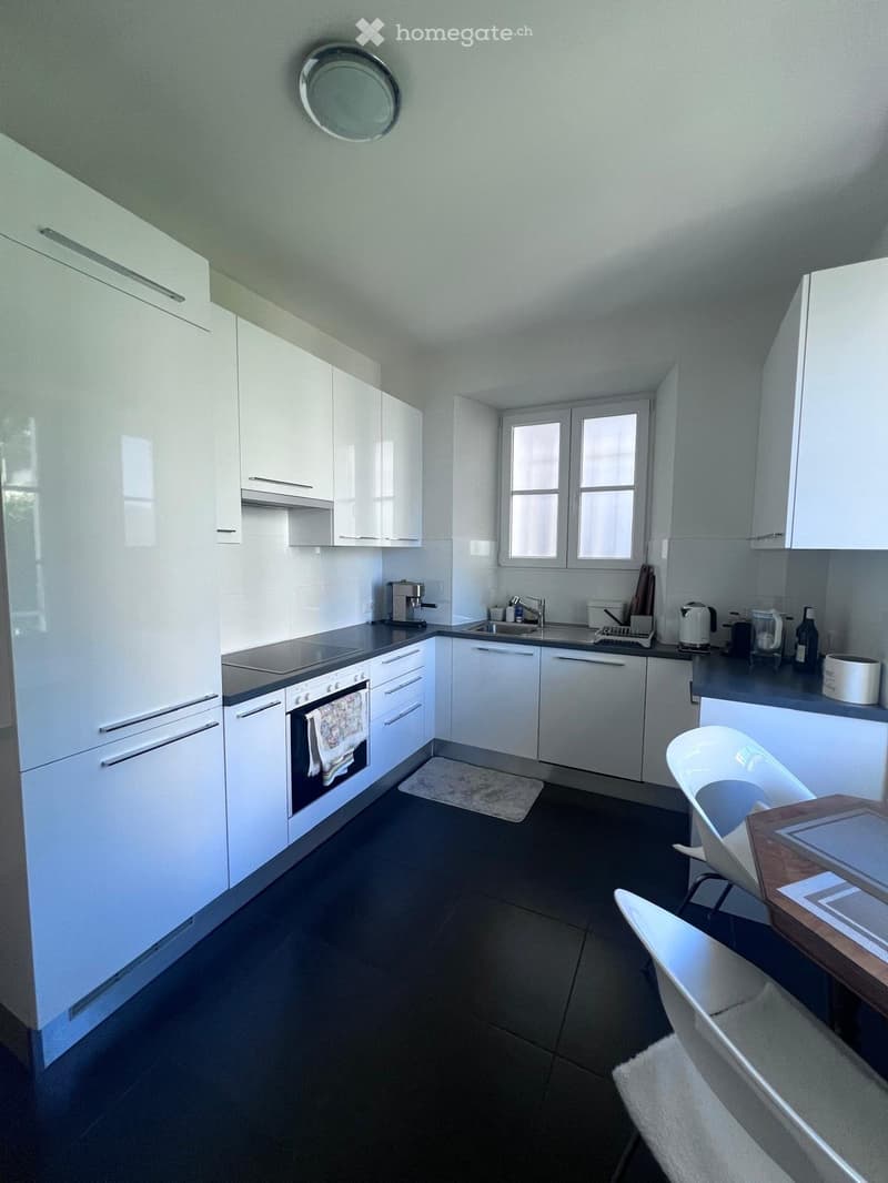 modern kitchen with white cabinets, black countertops, built-in oven, dishwasher, sink, faucet, coffee machine, kettle, toaster, and a window