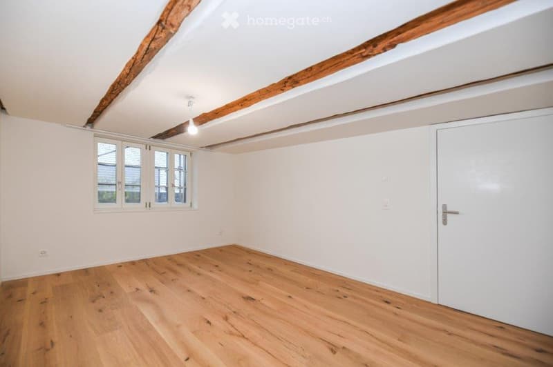 empty room with wooden floor, white walls, wooden beams, window