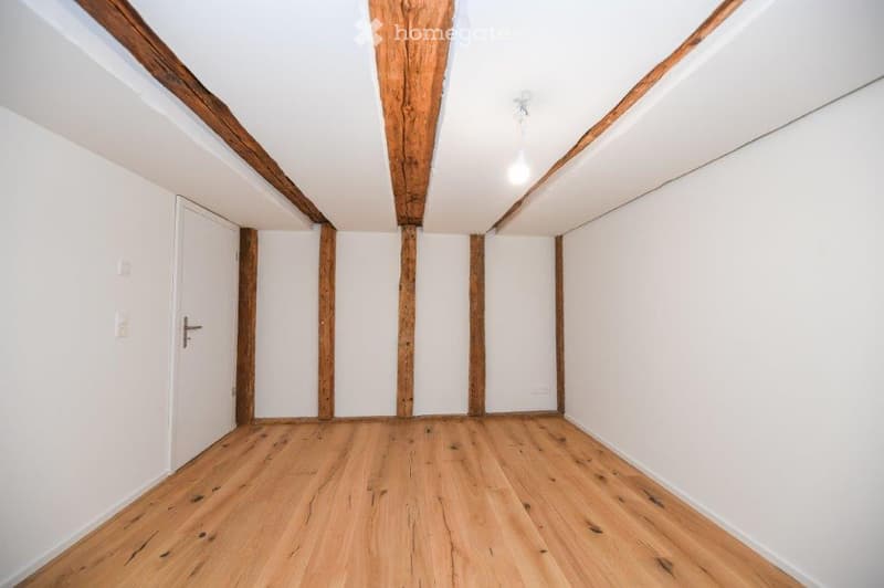 empty room, wooden beams, wooden floor, white walls, white door, light fixture