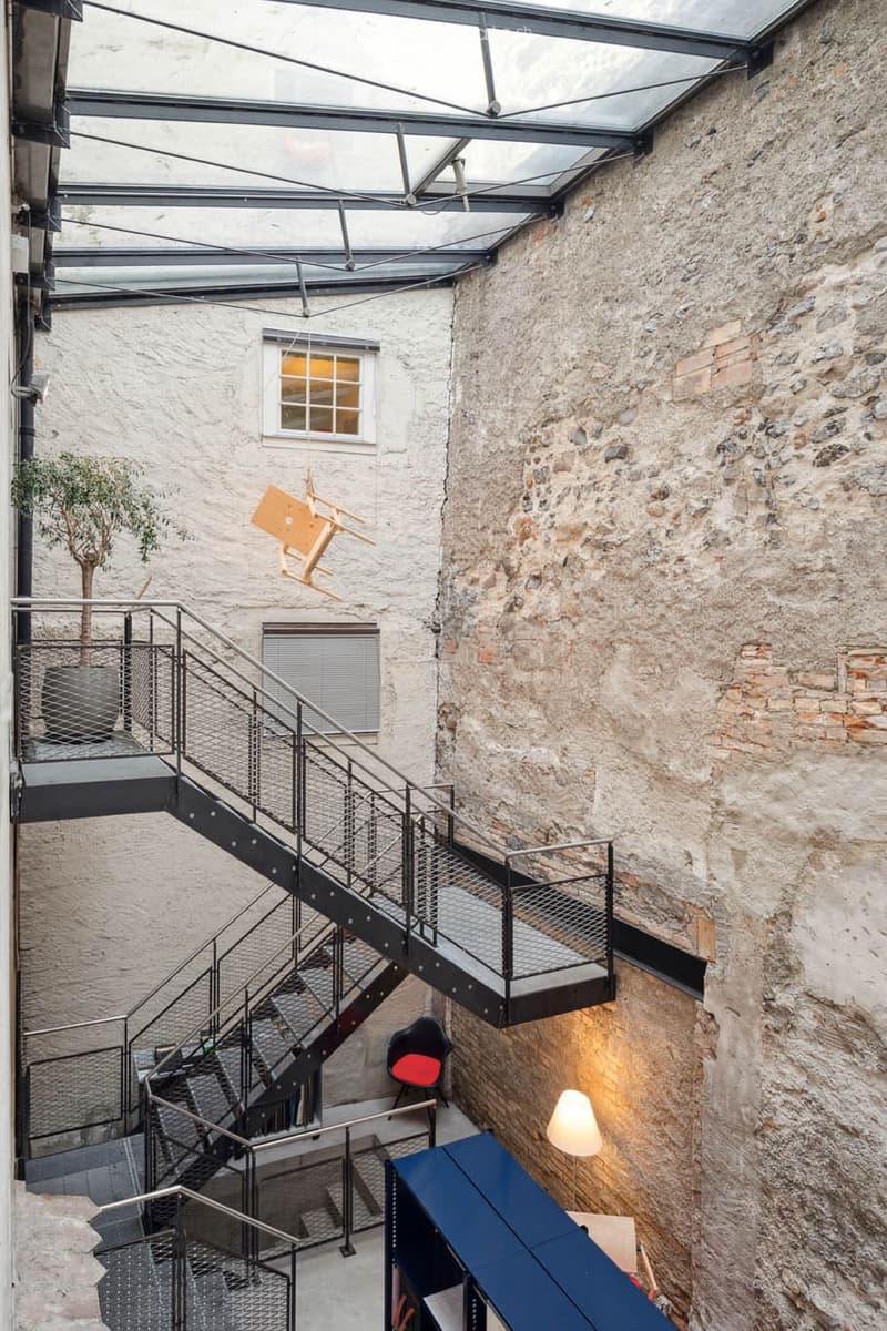 Modern staircase with metal railings and steps, interior view of a courtyard with exposed brick walls, hanging wooden object, hanging lamp.