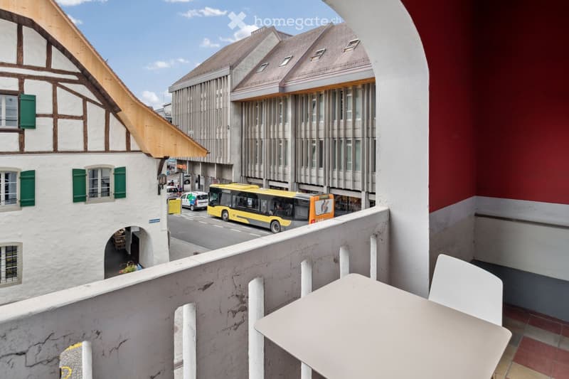 balcony, street view, buildings, yellow bus, white car, table and chair on balcony