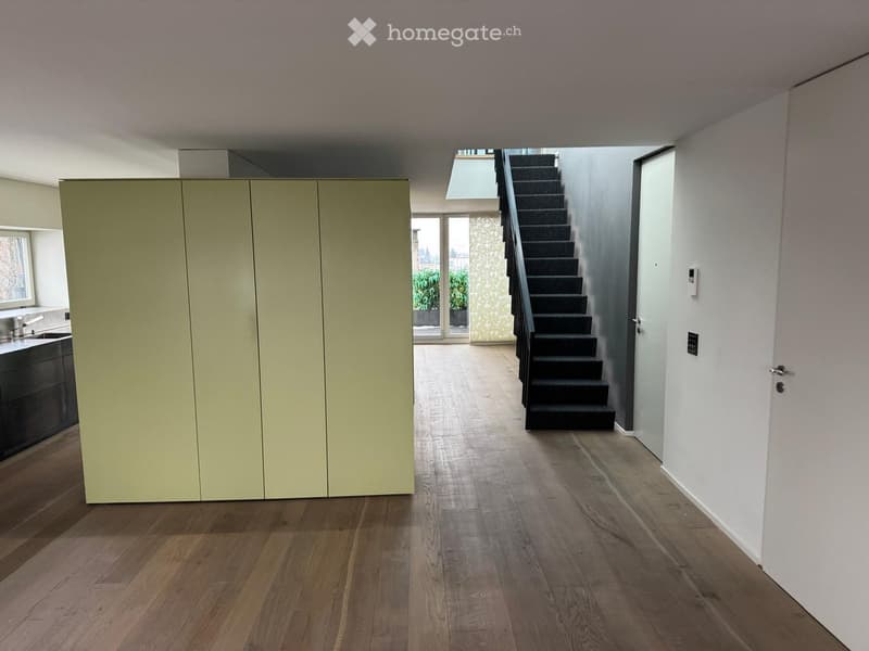Empty room with wooden floor, white walls, a large wardrobe, a staircase, and a glass door leading to a balcony.