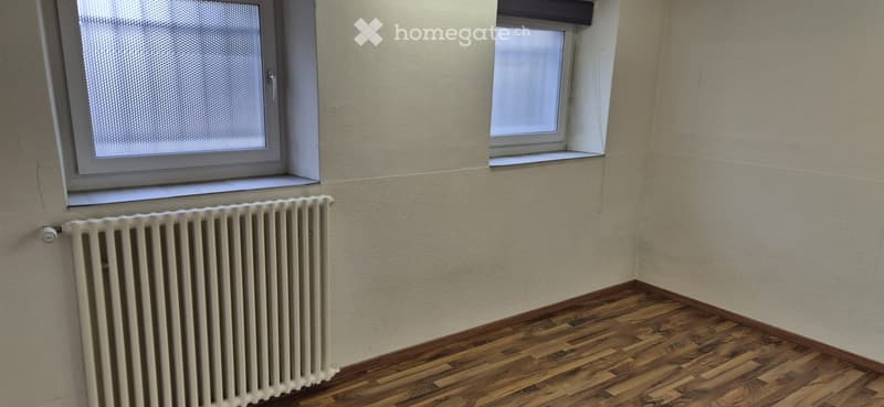 Empty room with wooden floor, white walls, two windows, and a white radiator
