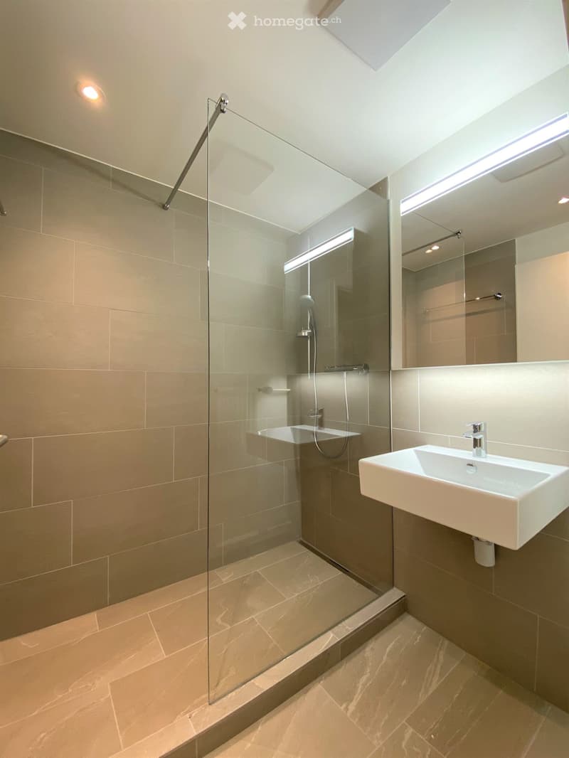 modern bathroom with glass shower enclosure, white sink, beige tiles, mirror, shower head, and towel rack