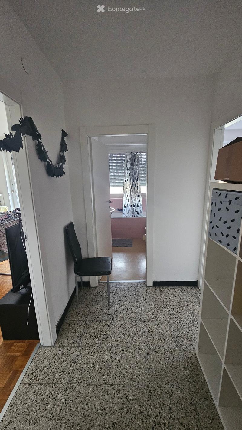 Empty room with chair, white walls, granite floor, open door to another room with bathtub