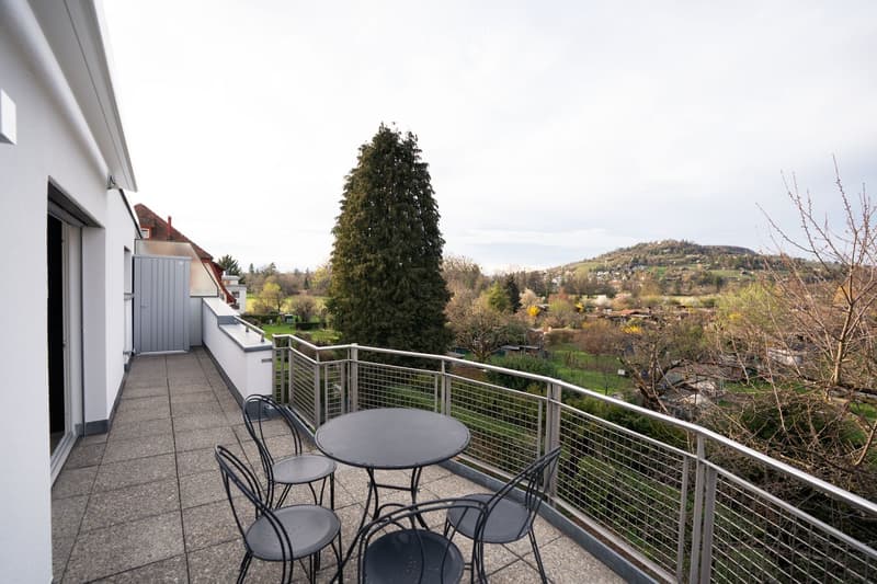 Balcony with table and chairs, metal railing, paved floor, view of trees and mountains