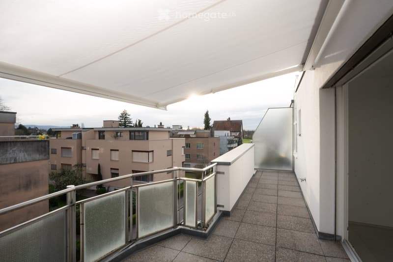 Balcony with glass railings, tiled floor, retractable awning