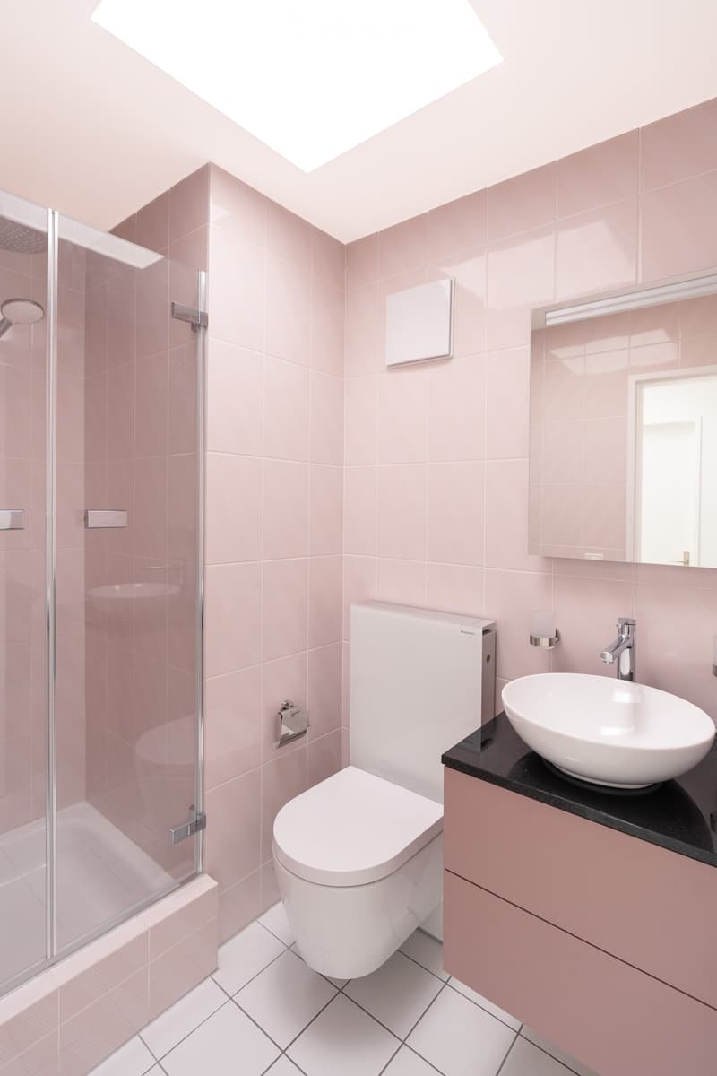 modern bathroom with pink tiles, glass shower enclosure, white toilet, white sink, mirror, black countertop