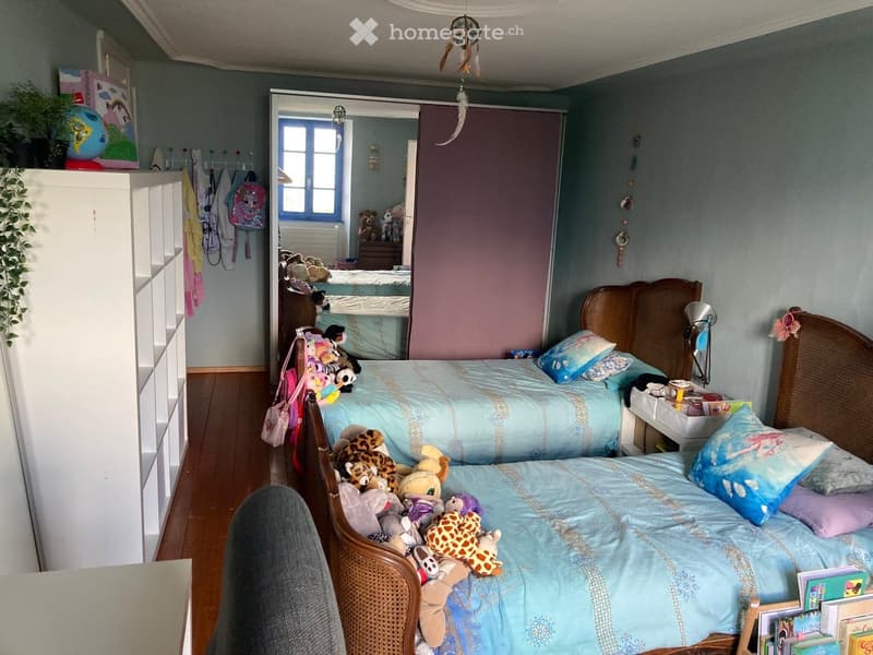 Two beds, wooden headboards, stuffed toys, white wardrobe, wooden floor, blue walls, window, dream catcher, plant