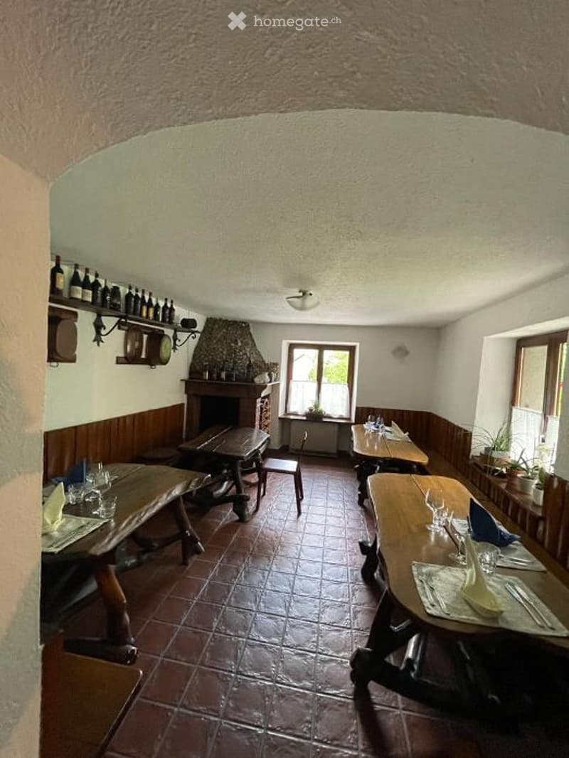 Dining room with wooden tables, chairs, fireplace, shelves with bottles, and windows