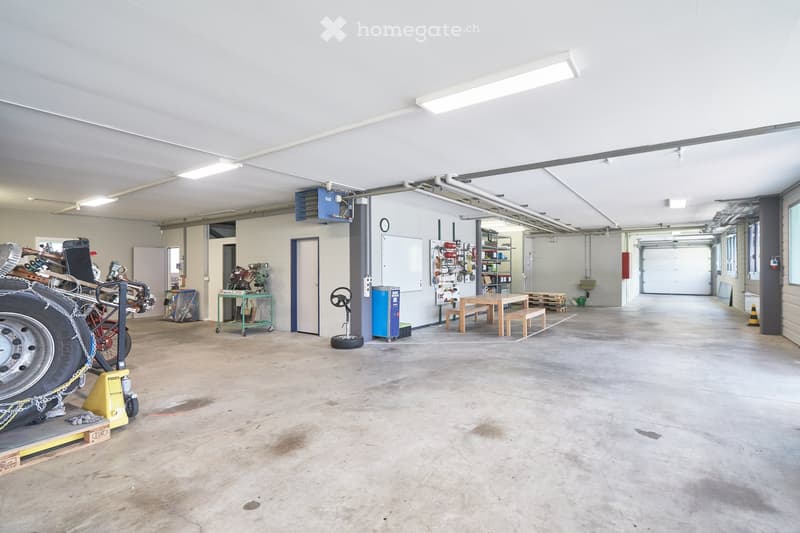large empty garage, white walls, ceiling lights, wooden table, benches, equipment, tires, metal stands