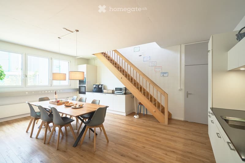 Dining room with wooden floor, dining table, chairs, kitchen with appliances, staircase