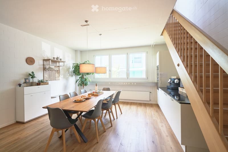 Dining room with wooden table, chairs, white walls, wooden floor, white cabinets, hanging lamps, staircase