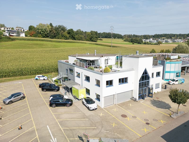 Modern white building with multiple windows, garage, and parking lot with several cars parked