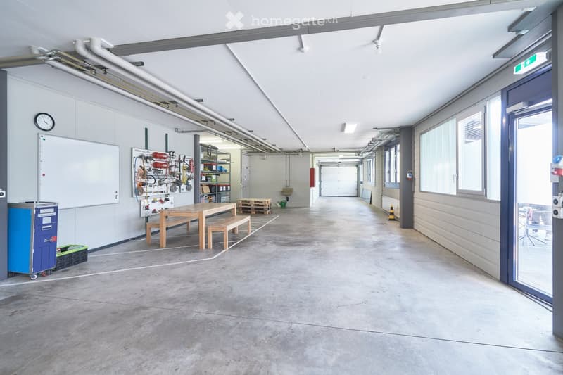 Empty room with white walls, concrete floor, wooden table and bench, whiteboard, clock, shelves with various items, and a door.