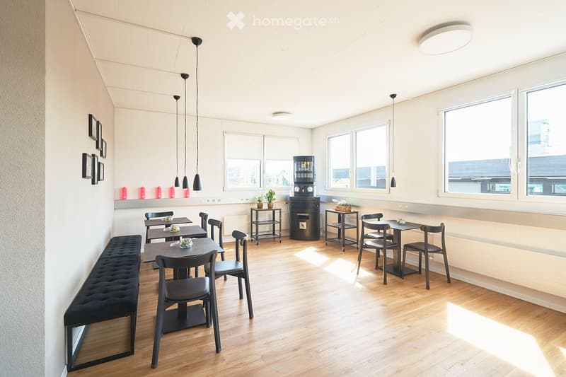 Dining area with wooden floor, black chairs, tables, bench, pendant lights, coffee machine, plants, large windows