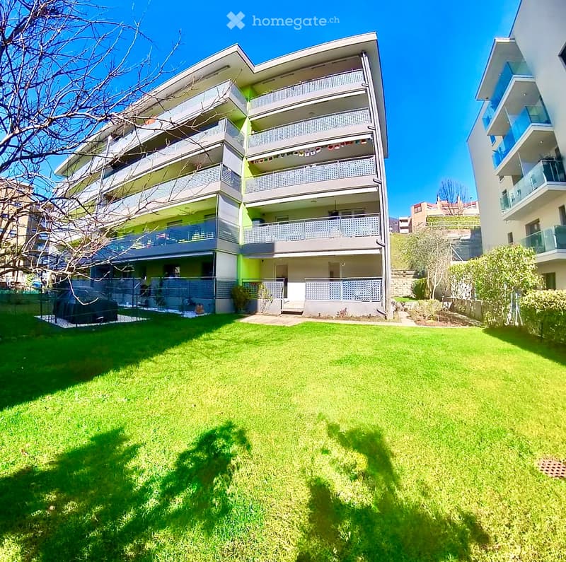 Modern apartment building with multiple balconies, green lawn, and a covered car parking area.