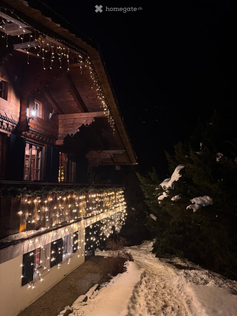 wooden chalet, balcony with lights, snow on the ground, trees