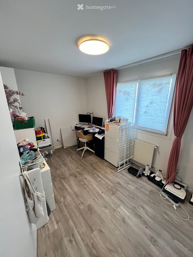 room with desk, monitors, chair, radiator, storage boxes, bags, and a bag hanging on the wall