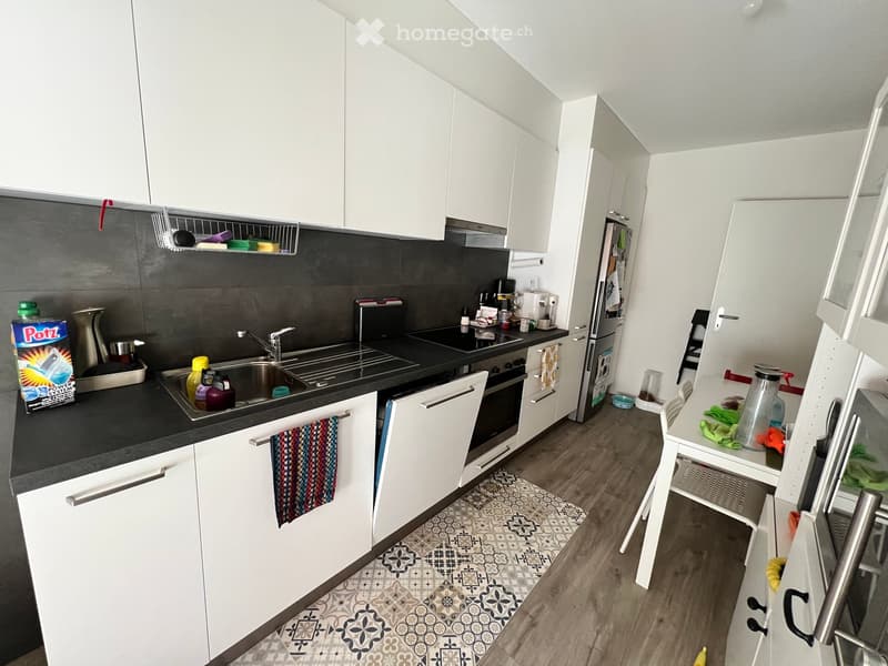 modern kitchen with white cabinets, black countertops, stainless steel sink, dishwasher, refrigerator, and a small dining area