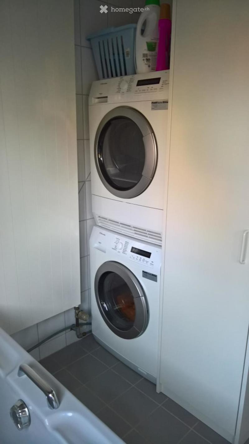 Stacked washer and dryer, white cabinets, bathtub, tiled floor